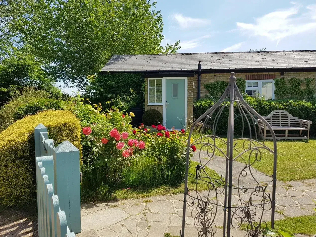 The farm cottage near Ash, East Kent where Anna holds in-person sessions — a sage-green door framed by roses and a garden arch