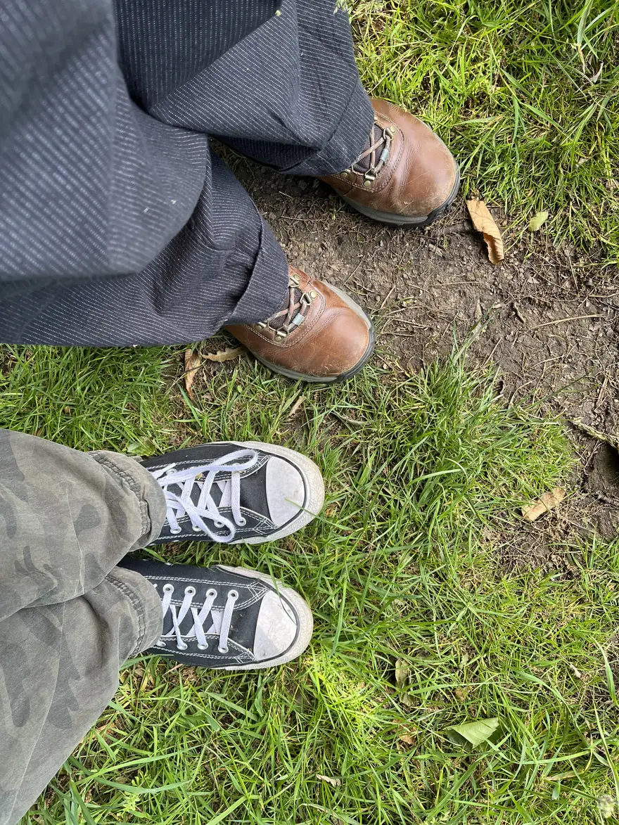 Two pairs of shoes — walking boots and trainers — side by side on a grassy path, out together for a walk